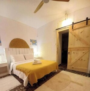 Een slaapkamer met een bed, nachtkastje, houten deur en een plafondventilator.