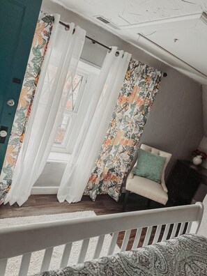 A room with a white chair, a floral curtain, and a view of a building outside. - Historic 11BR Home – Ride to Hatfield-McCoy - Historic 11BR Home – Ride to Hatfield-McCoy (Williamson)