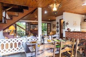 Uma sala de jantar com móveis de madeira, uma escada e uma cozinha visível ao fundo.