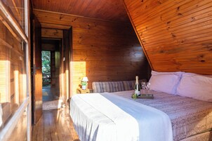 Quarto de cabana de madeira com cama, mesa de cabeceira e janela.