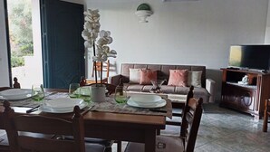 A dining area with a table set for four, a sofa with patterned cushions, and a television on a wooden stand. - Welcomely - Casa San Pietro (Budoni)