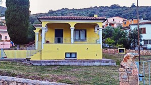 A yellow building with a balcony, surrounded by stone walls and other buildings. - Welcomely - Casa San Pietro (Budoni)