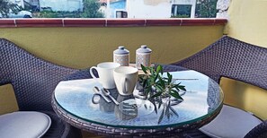 Una mesa redonda de vidrio, una silla de fibras naturales y cojines, una planta en maceta y dos recipientes decorativos.