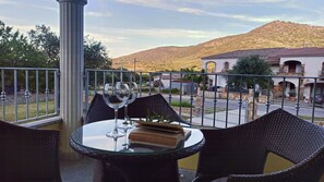 A balcony with wicker chairs and a glass table, overlooking a street and a hill. - Welcomely - Casa San Pietro (Budoni)