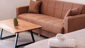 A modern living room with a brown sofa, a wooden coffee table with a cactus, and a neatly folded white towel on a bed. - Horizon 4 You Mykonos (Mykonos)