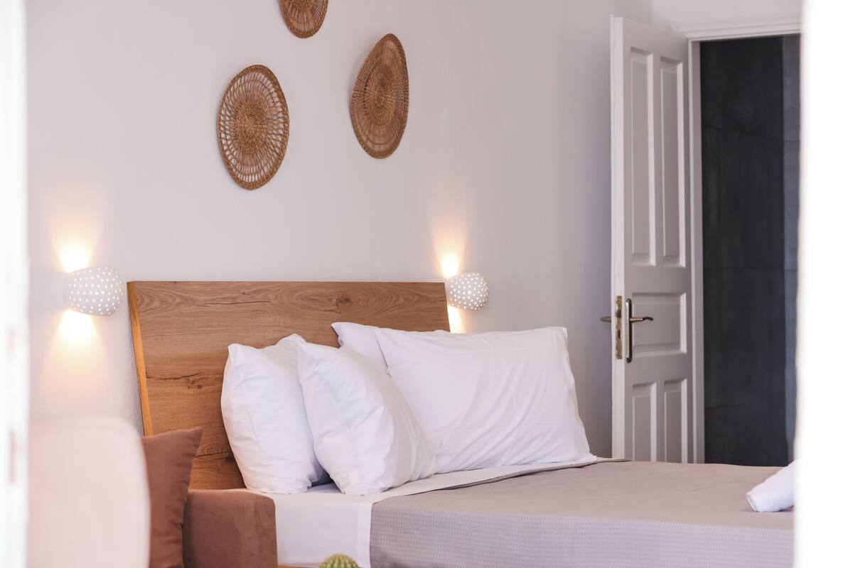 A neatly made bed with white and brown bedding, a wooden headboard, and two wall-mounted light fixtures.