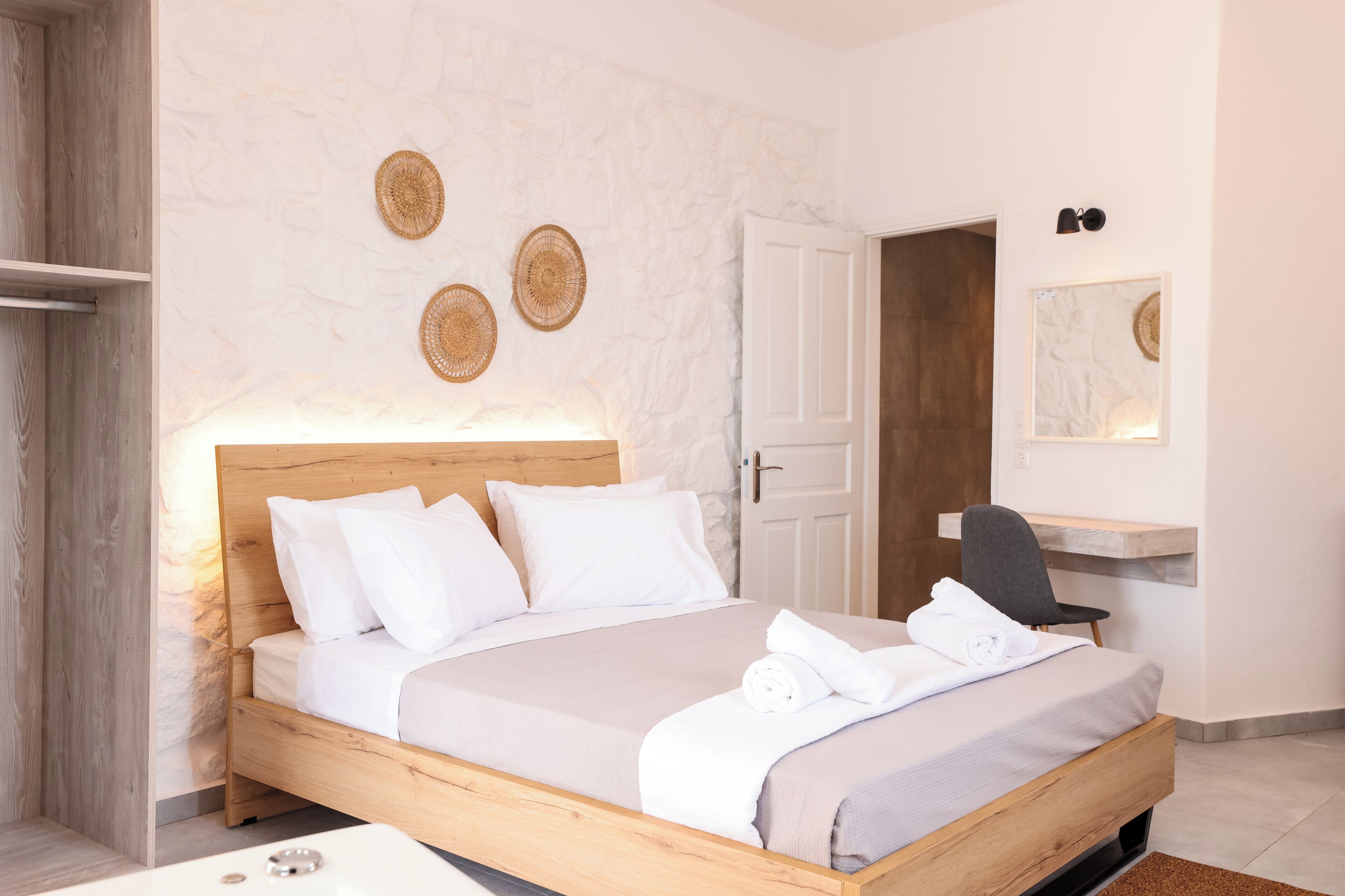 Une chambre moderne avec un lit en bois, une literie blanche, une table de chevet, une chaise et un miroir fixé au mur.