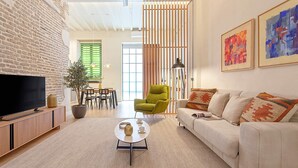 Un saló modern amb una paret de maó, un televisor de pantalla plana, un butac armchair verd, un sofà blanc i quadres abstractes.