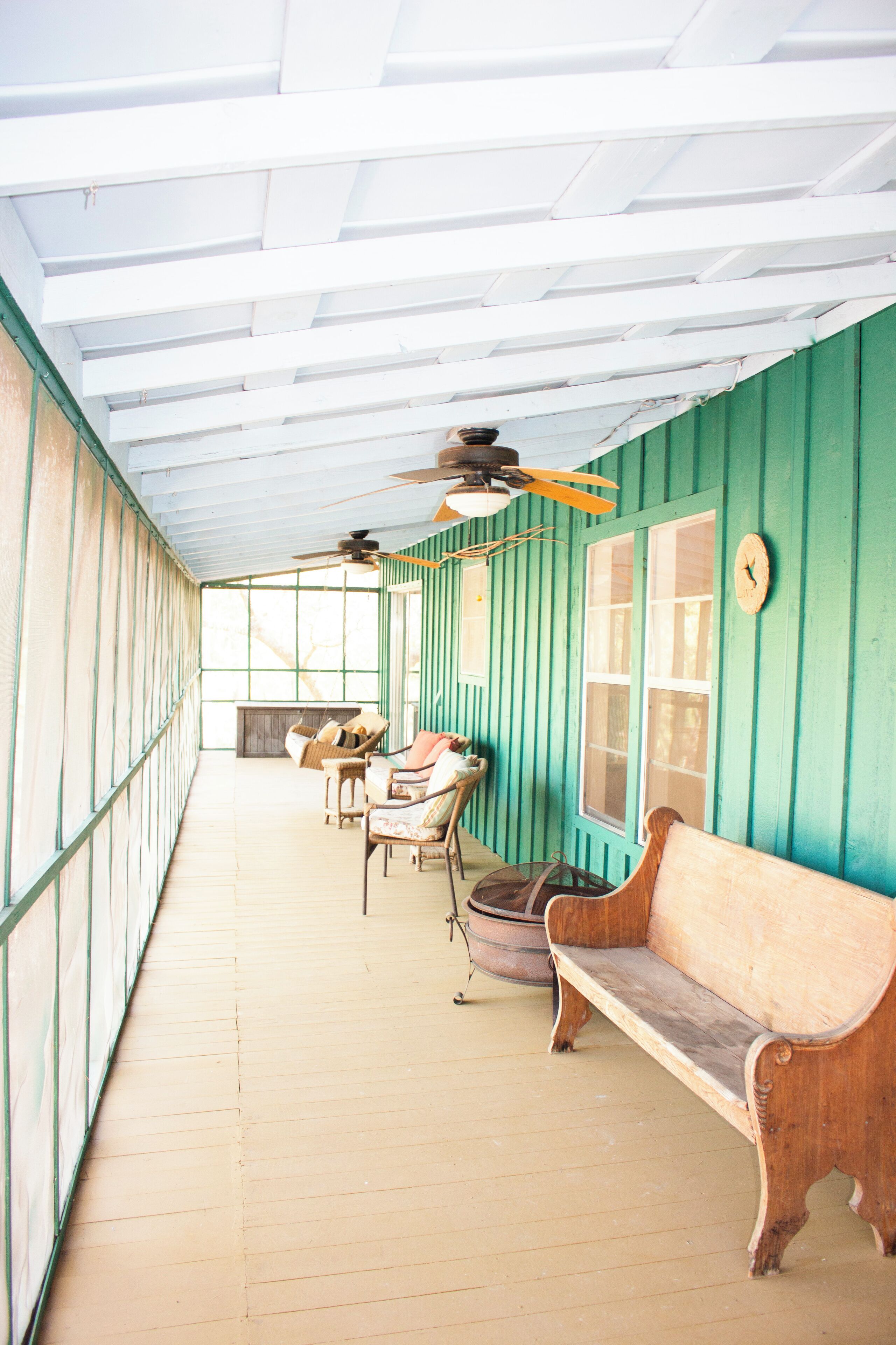 A covered porch with wooden benches and chairs, a ceiling fan, and a large window.