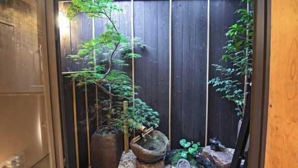 Un jardín japonés tradicional con valla de madera, faroles de piedra y diversas plantas.