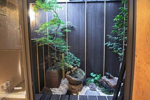 Ein traditioneller japanischer Garten mit einem hölzernen Tor, einem steinernen Laternenpfosten und einem kleinen Baum.