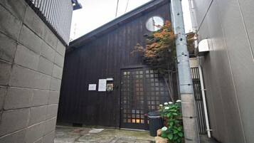 A narrow alleyway with a wooden building, a metal gate, and a small tree.