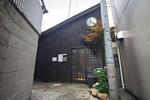 Une ruelle étroite avec un bâtiment en bois, une porte en métal et un petit arbre.