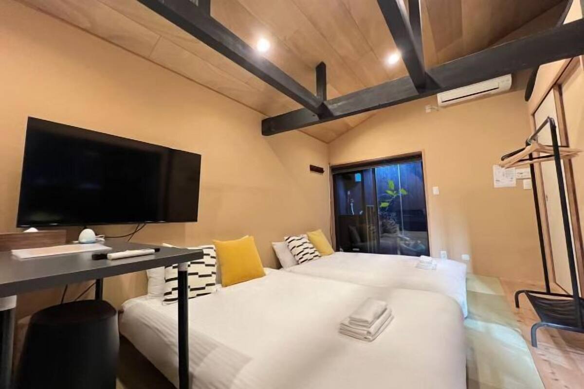 Habitación de hotel con cama, escritorio, televisor de pantalla plana, ventana y perchero.