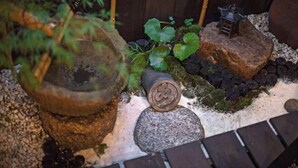 Un jardín con una planta en maceta, una piedra y una figurita sobre una roca.