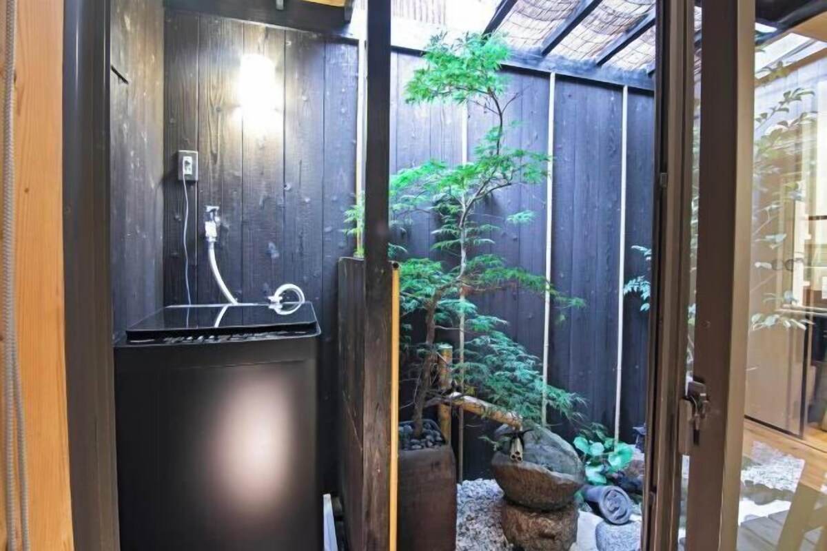 A traditional Japanese-style room with tatami flooring, a shoji screen door, and a small indoor garden with a bonsai tree and rocks.