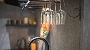 Una cocina con un grifo moderno, una cafetera y copas de vino colgando.