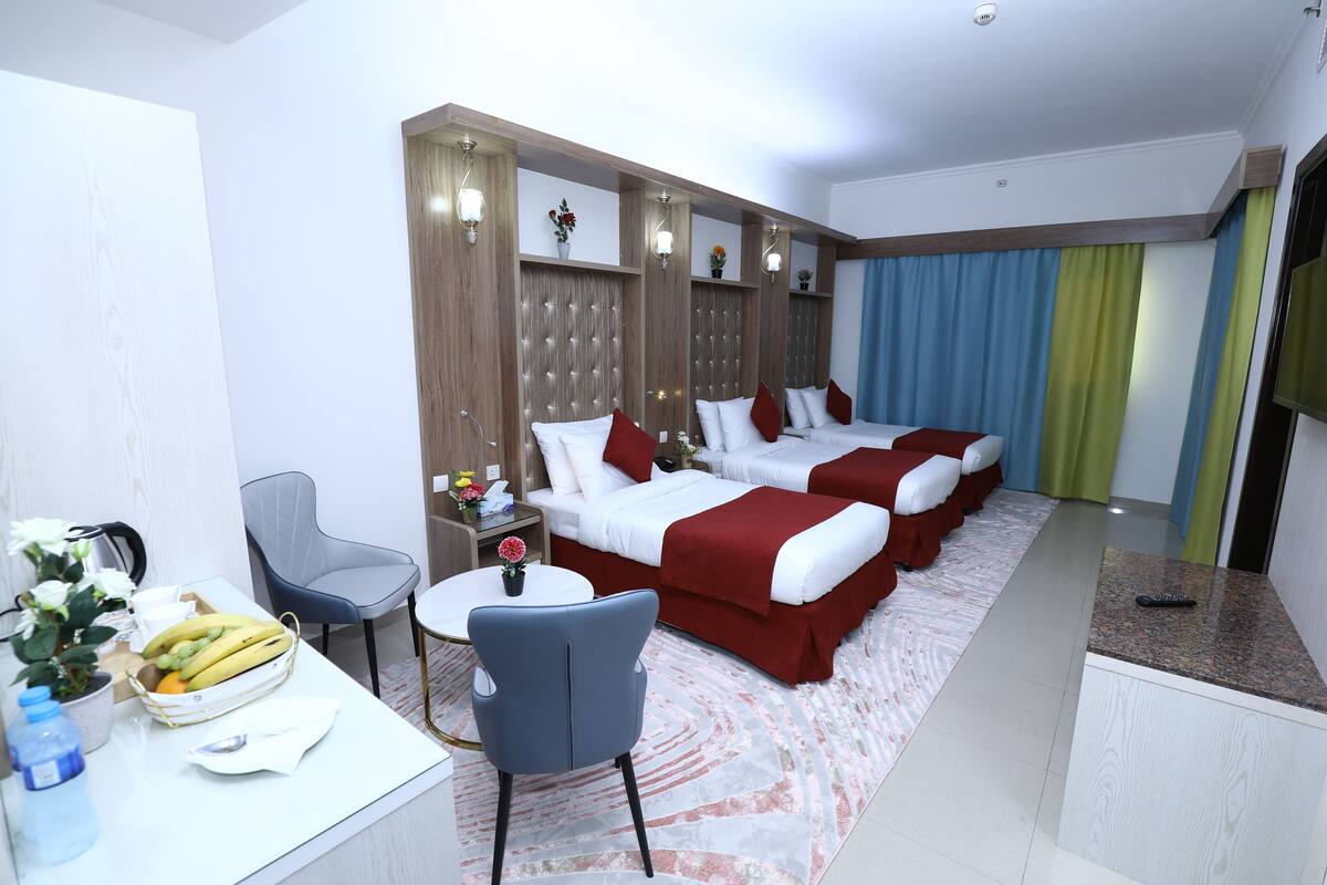 A hotel room with two beds, a desk with a chair, a small table, and a potted plant.