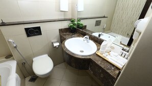 A compact bathroom with a white toilet, a sink with a marble countertop, a handheld showerhead, and a small potted plant. - Naif Fort Hotel  (Dubai)