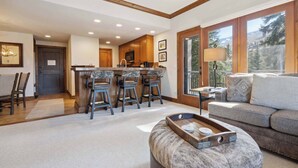 A spacious living area with a large window, a kitchen with wooden cabinets, and a bar area with stools.