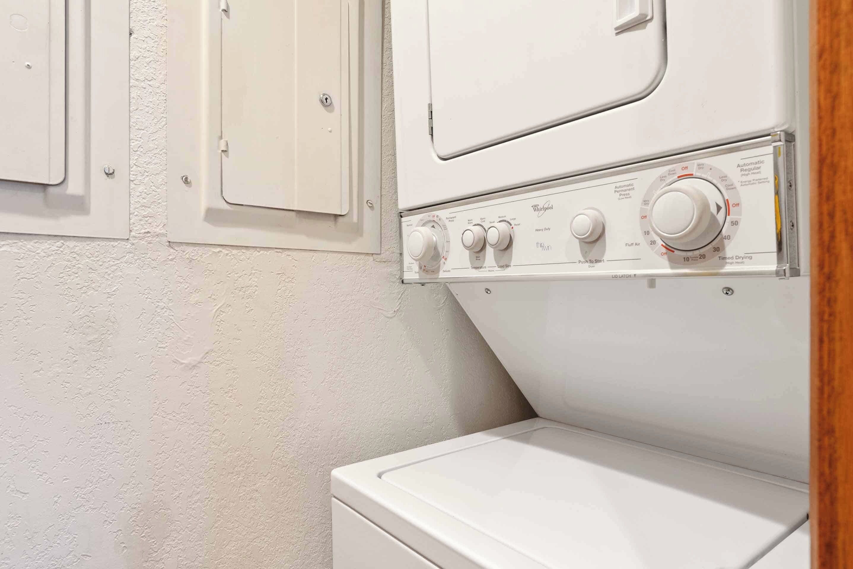 A white washing machine with control knobs and a door, mounted on a textured wall.