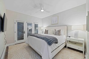 A bedroom with a bed, bedside tables, a ceiling fan, and a door with glass panels.