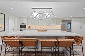 A modern kitchen with a large island, white cabinets, and a unique chandelier.