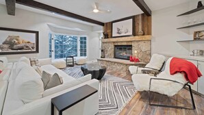 A modern living room with a fireplace, white furniture, and a view of trees through large windows. - The Charter at Beaver Creek E2405 (Beaver Creek)