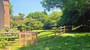 A wooden fence with a gate, a brick building, and lush green trees in the background. - Gracious Lower Level Family Suite (Oakton)