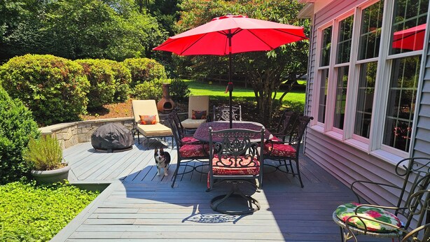 A wooden deck with outdoor furniture, including a table and chairs, and a red umbrella. - Gracious Lower Level Family Suite (Oakton)