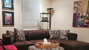 A living room with a brown sofa, patterned ottoman, and a basket with tissues. - Gracious Lower Level Family Suite (Oakton)