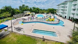A swimming pool area with a water slide, lounge chairs, and a building with balconies. - Seaside Inn - in Litchfield (Pawleys Island)