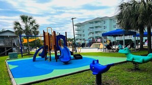 A playground with slides and climbing structures, surrounded by grass and palm trees. - Seaside Inn - in Litchfield (Pawleys Island)