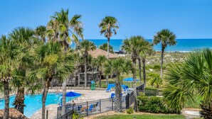 A pool area with palm trees, a fenced deck, and a view of the ocean.