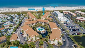 An aerial view of a resort with a central pool, beachfront promenade, and a beach walkover.
