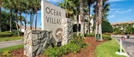 A sign for Ocean Villas with a stone base and a palm tree in the background.