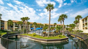 A resort with a central water feature, palm trees, and a pool area with umbrellas.