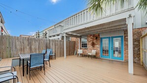 A wooden deck with outdoor furniture, a brick building with blue doors, and a wooden fence.