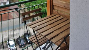 A balcony with a wooden bench, a view of a railway track, and buildings in the background.