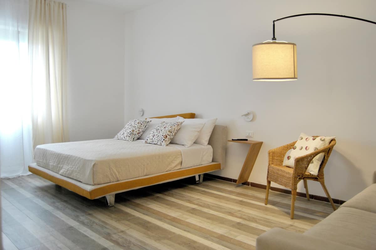 Quarto com cama, cadeira, mesa de cabeceira e luminária na parede.