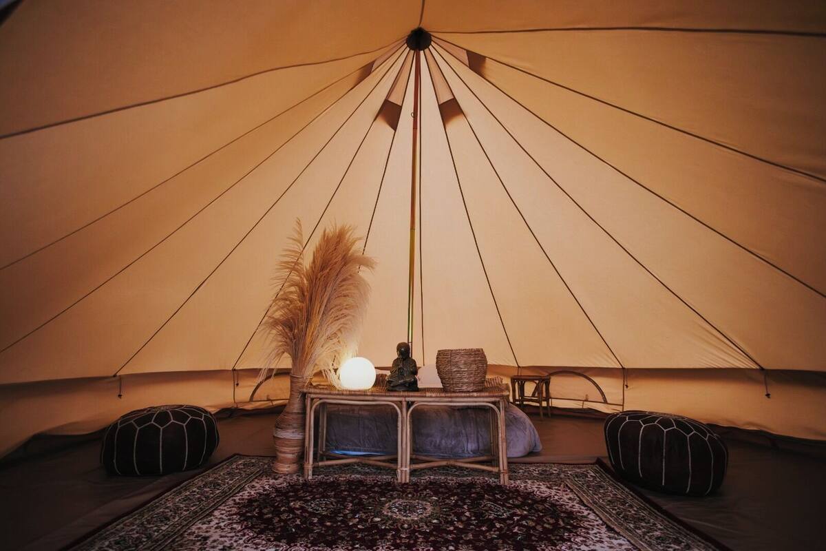 A tent interior with a central table, two chairs, a lamp, and decorative items.