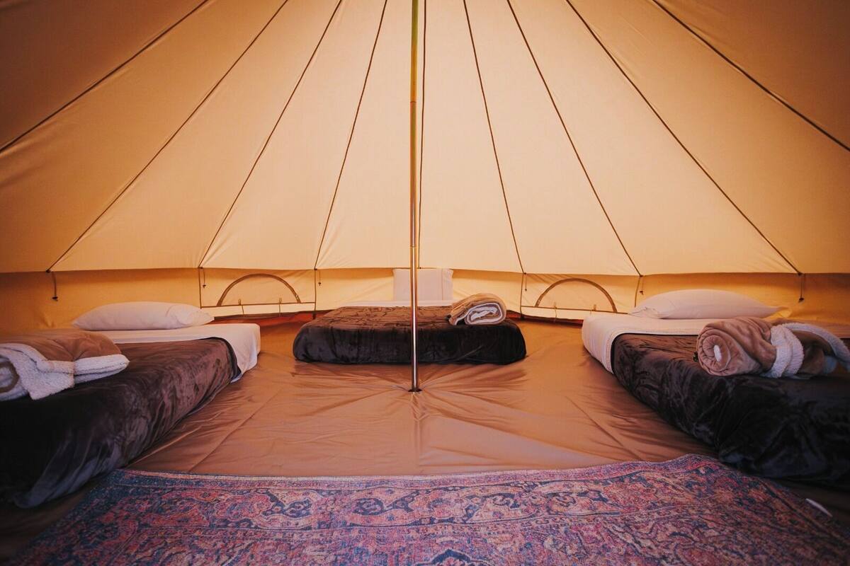A tent with three beds, each with a pillow and a rolled towel.
