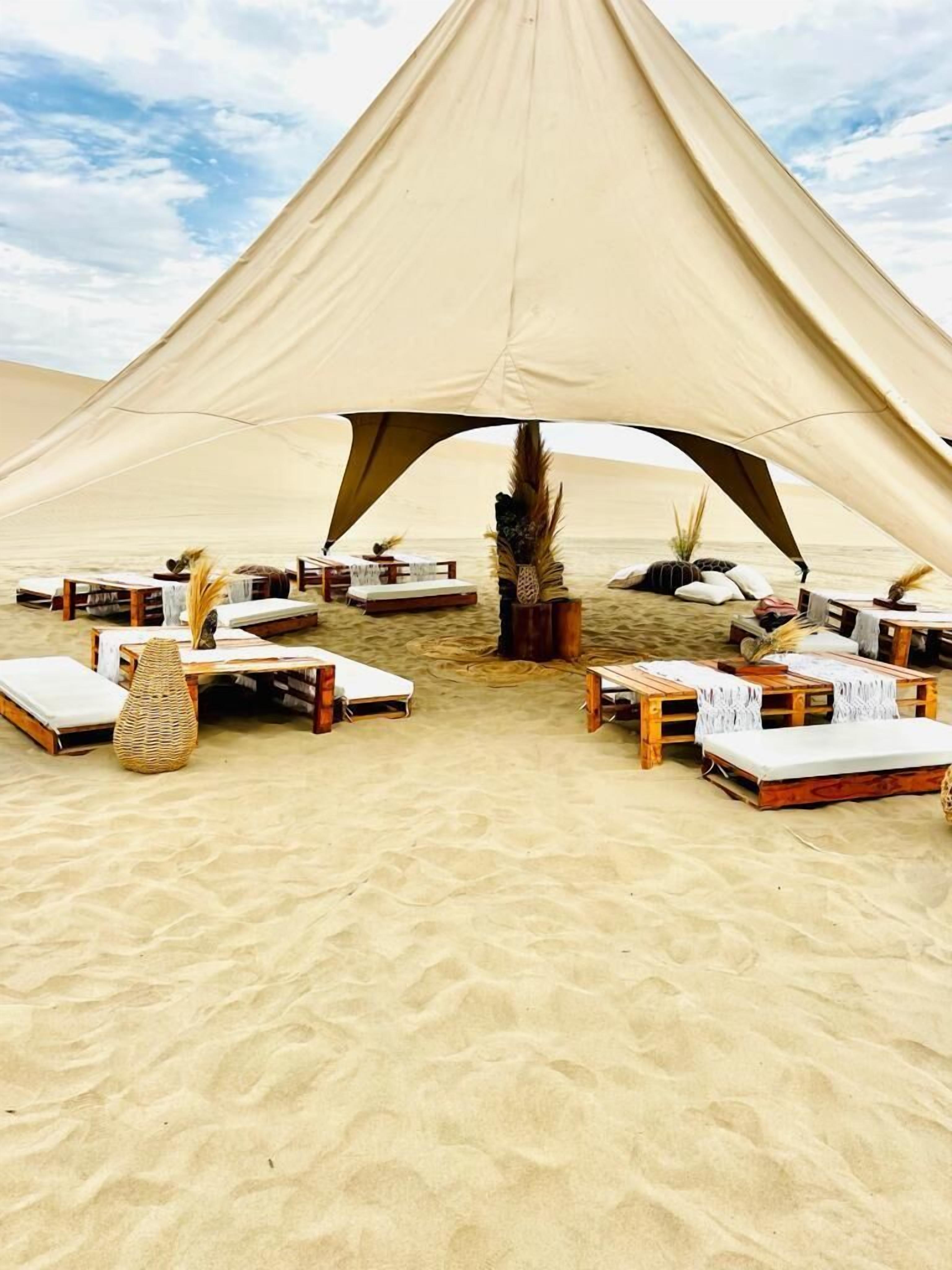 Una tienda de campaña en el desierto con varias zonas de descanso, cada una con un colchón y muebles de madera.