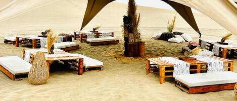 Una tienda de campaña en el desierto con varias zonas de descanso, cada una con un colchón y muebles de madera.