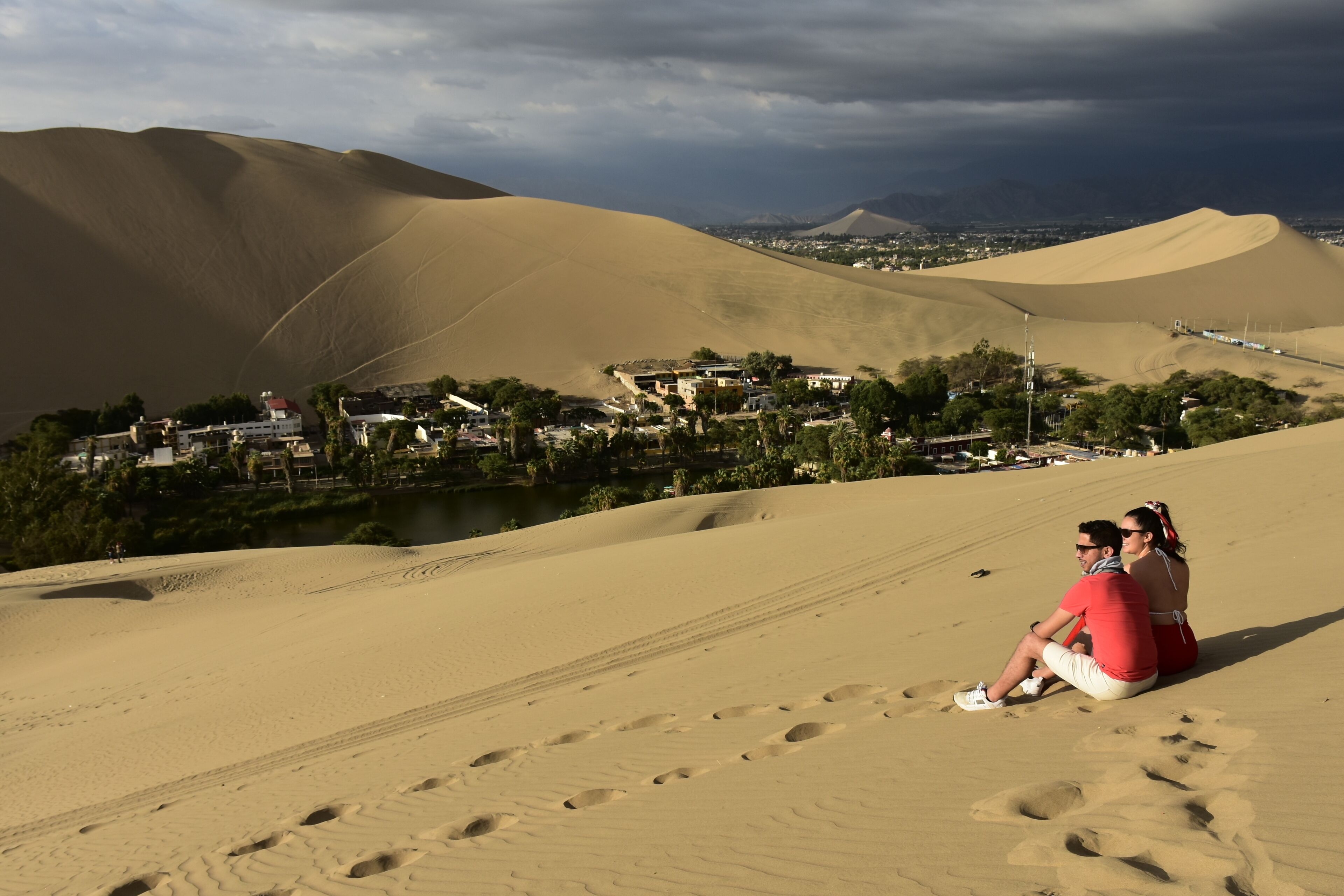 A desert landscape with sand dunes and a small settlement in the background.