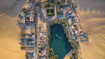 Vista aérea de un resort con piscina central, rodeado de edificios y dunas de arena.