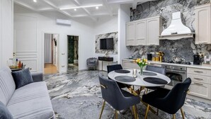 Una cocina moderna con encimeras de mármol, una zona de comedor con una mesa redonda y sillas, y una sala de estar con sofá.