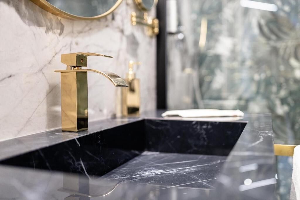 Une salle de bain moderne avec un lavabo en marbre noir et des accessoires dorés.