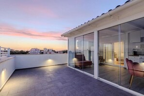 Un apartamento moderno con un cerramiento de vidrio corredera que da a un área de estar, un balcón con vistas a la ciudad y piso de baldosas.