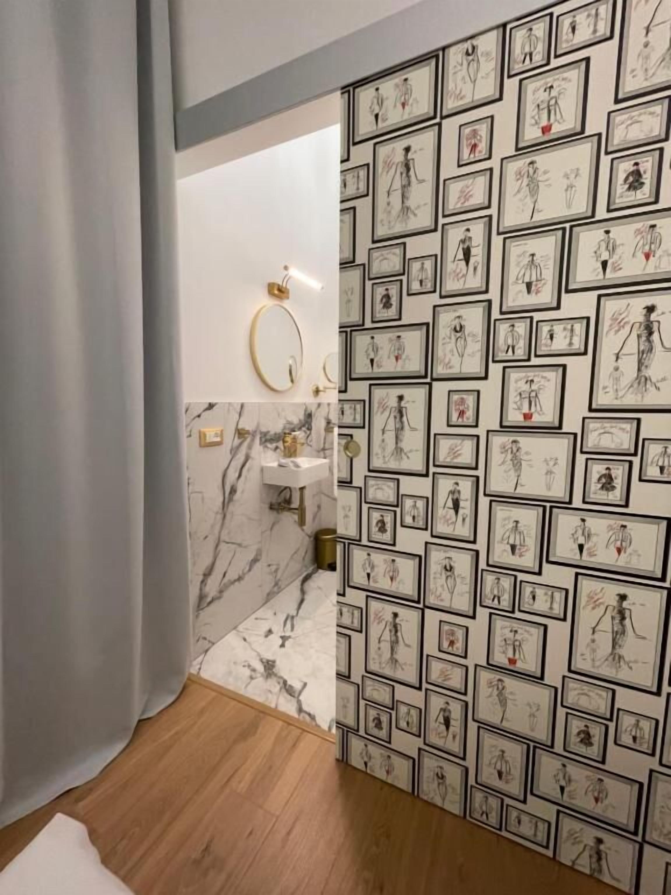 Un baño con piso de mármol, lavamanos y pared decorada con bocetos enmarcados.